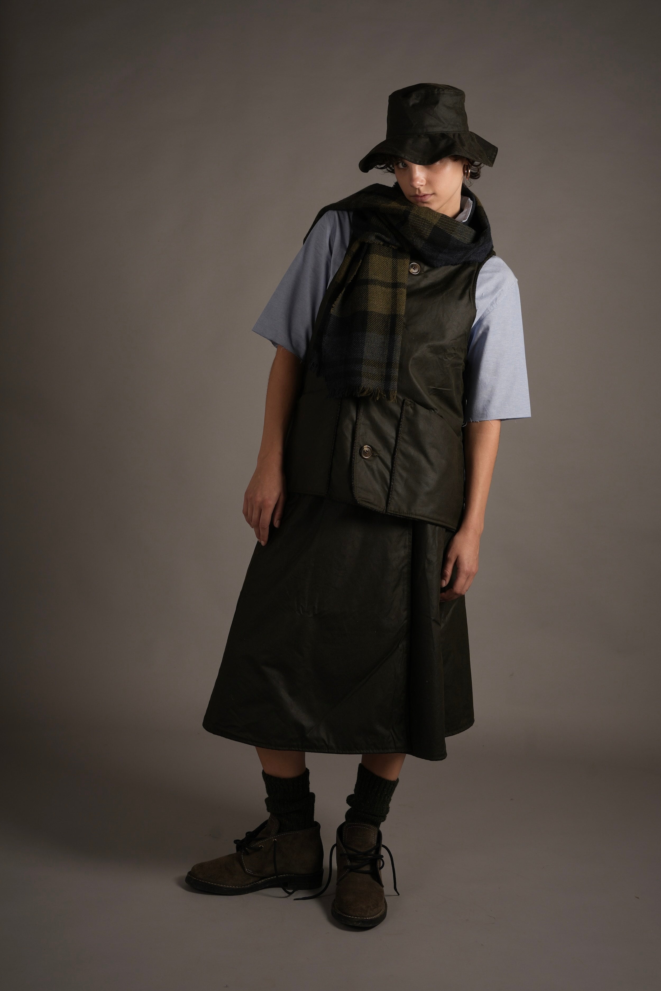 Els Wears Carrier Company Norfolk Wax Jerkin in Dark Olive with Wrap Skirt, Pinpoint Chambray Shirt And Wax Rain Hat
