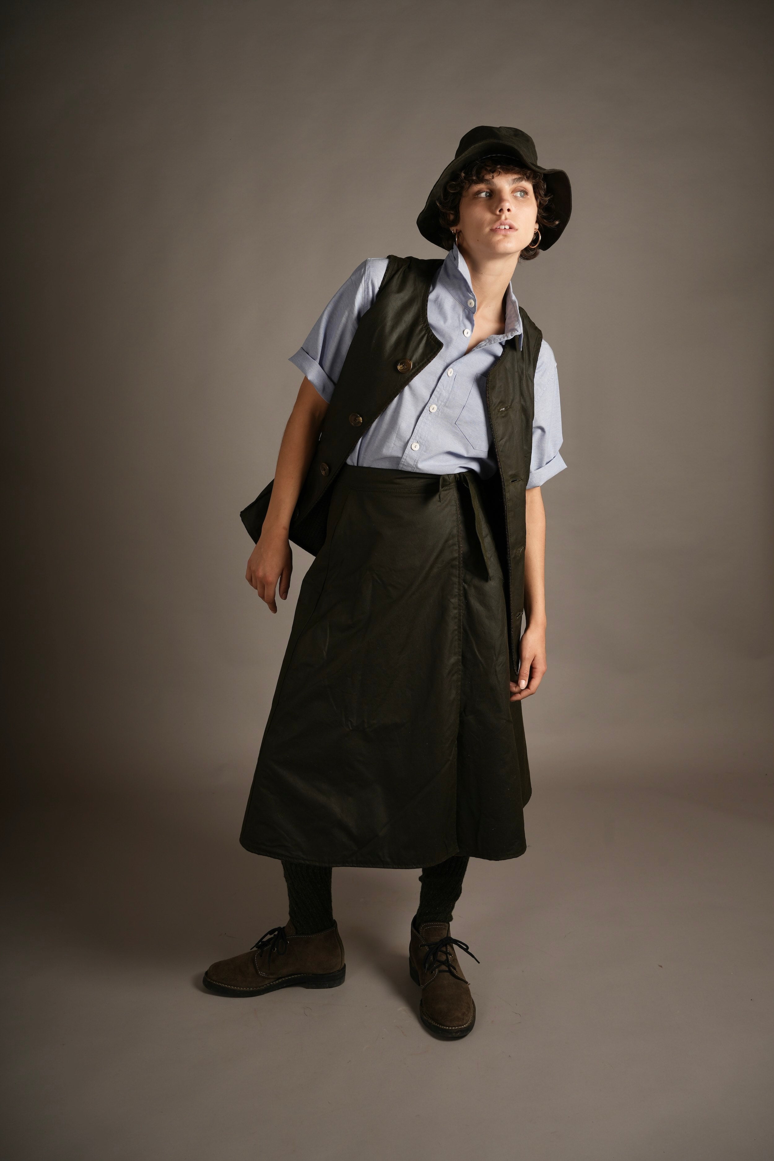 Els Wears Carrier Company Norfolk Wax Jerkin in Dark Olive with Wrap Skirt, Pinpoint Chambray Shirt And Wax Rain Hat