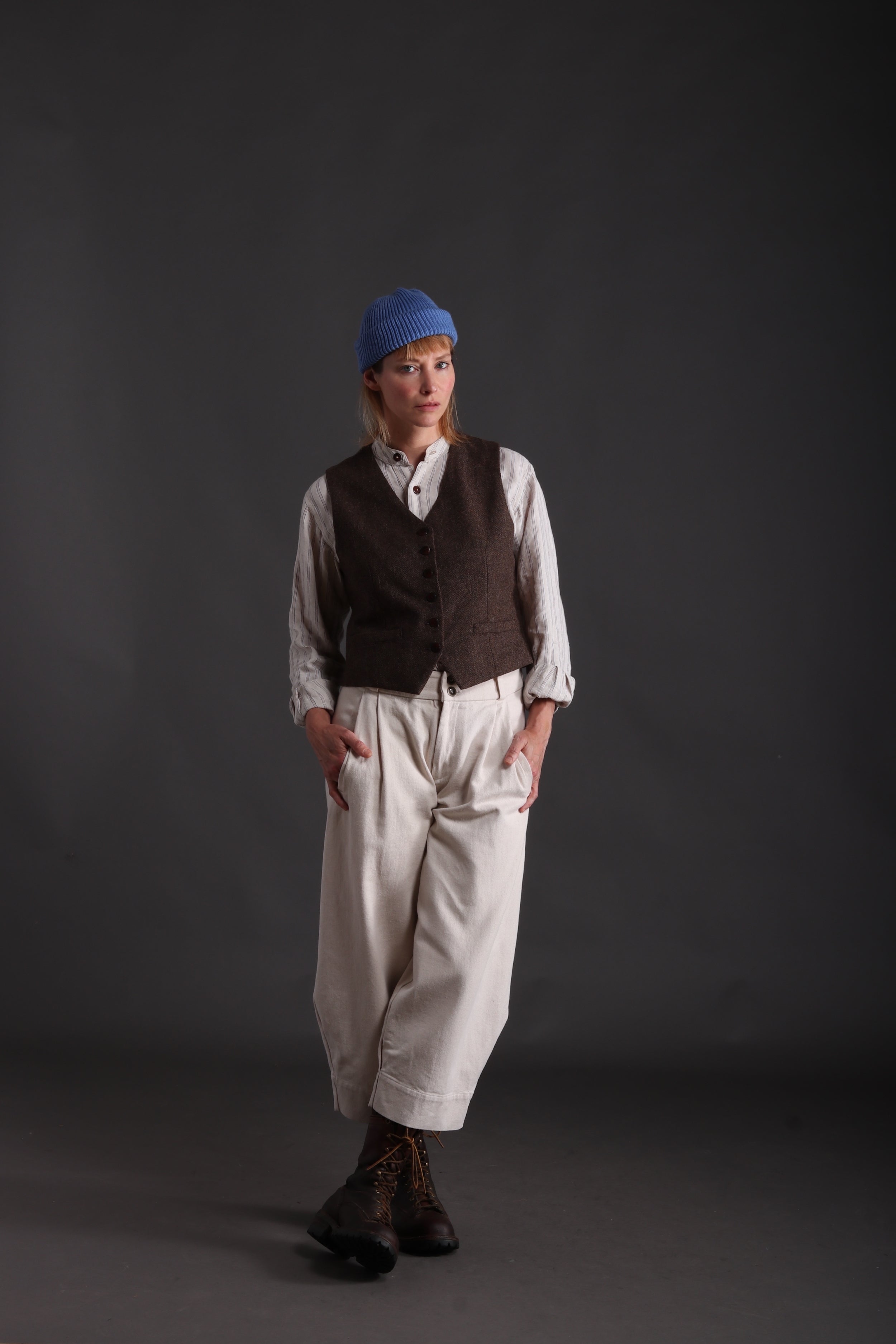 Woman wears Wool Waistcoat in Brown and Collarless workshirt with Seeded Denim Trousers and Donegal hat in Turquoise